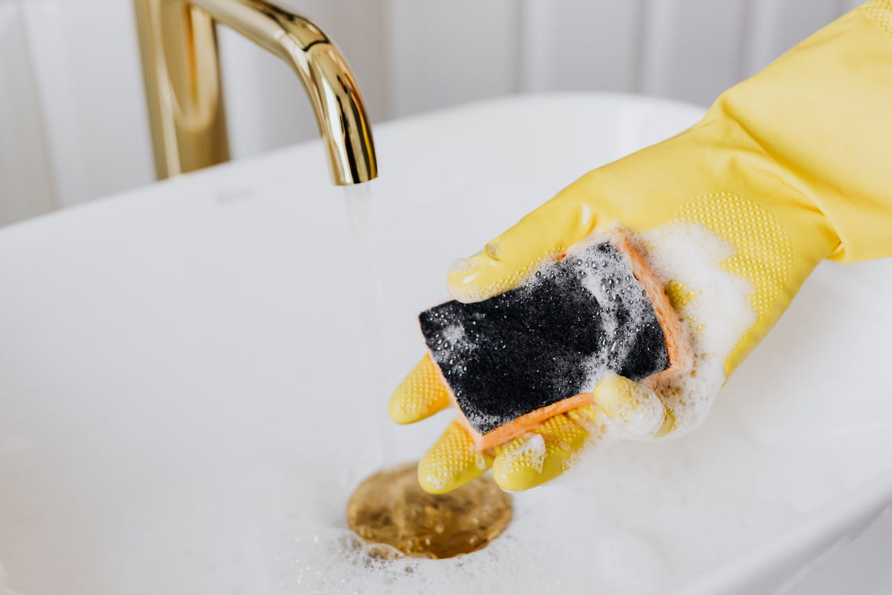 why-choose-us Crop faceless person in yellow latex protective glove using detergent and sponge while washing surface of white sink in bathroom