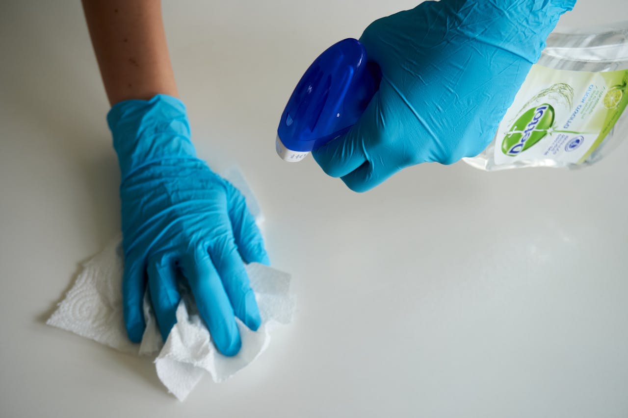 gallery-2 Close-up of hands wearing gloves cleaning a surface with disinfectant spray.