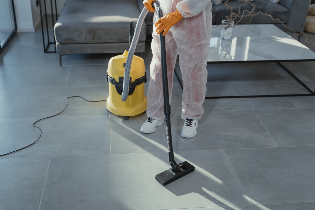 hero-img-01 A professional cleaner in protective gear vacuuming the floor in a modern living room.